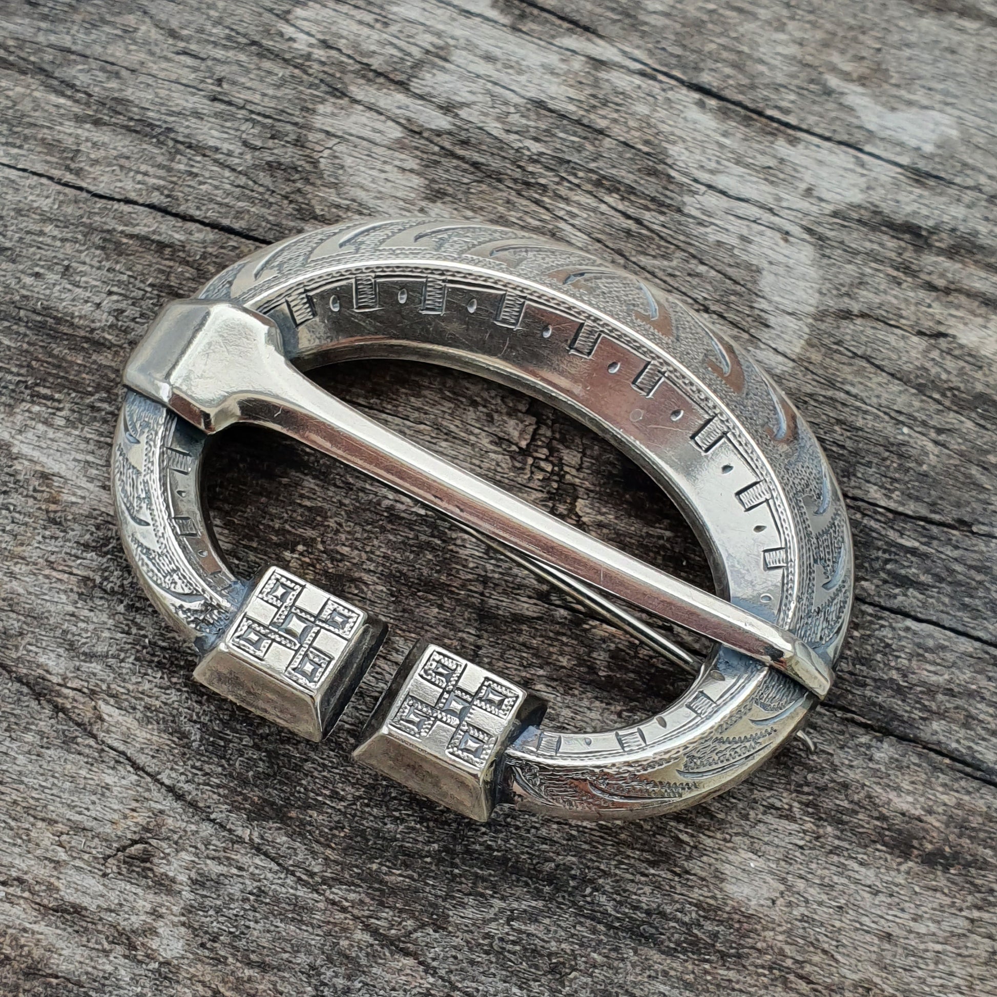 Silver Celtic-style brooch with engraved patterns and square end pieces.