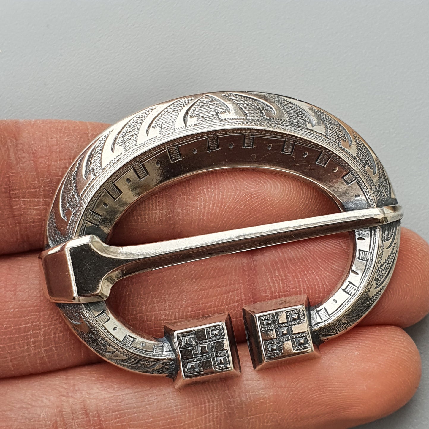 Ornate silver penannular brooch with decorative engraving and square end terminals.