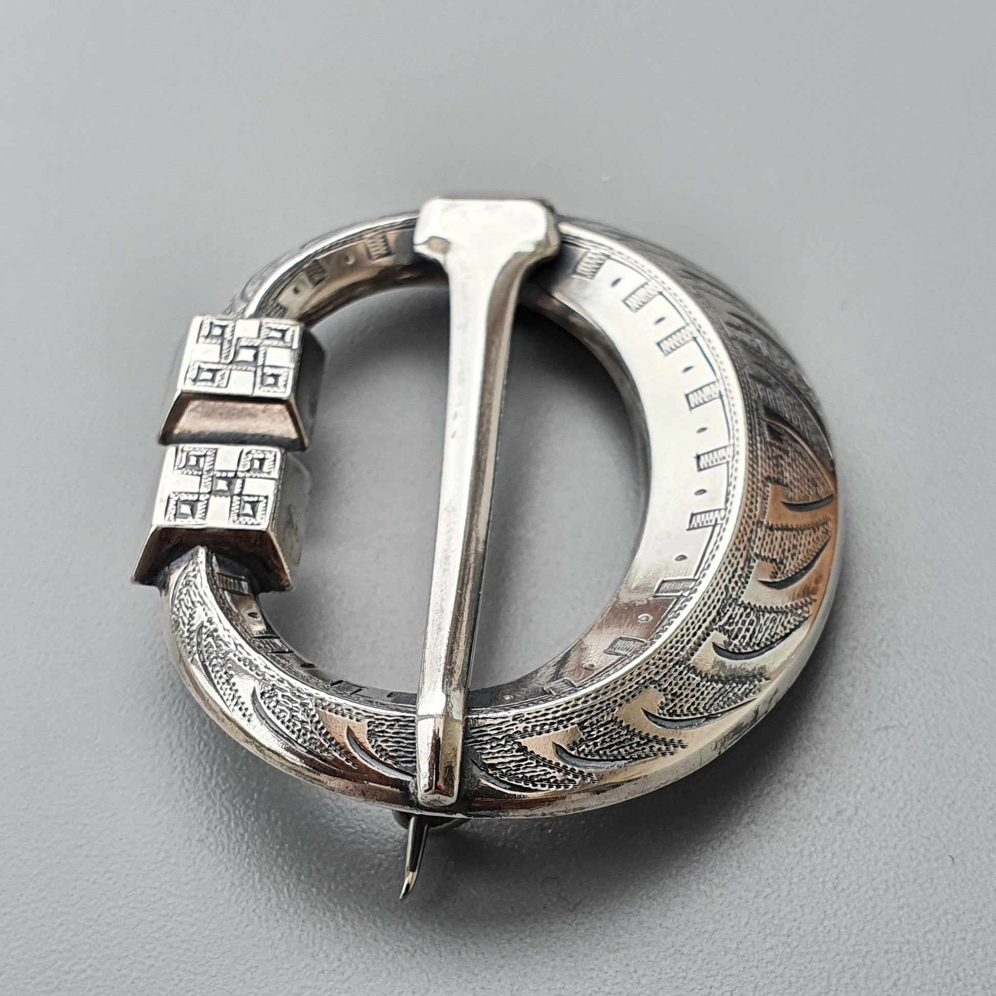 Ornate silver penannular brooch with intricate engraved designs and a decorative pin.