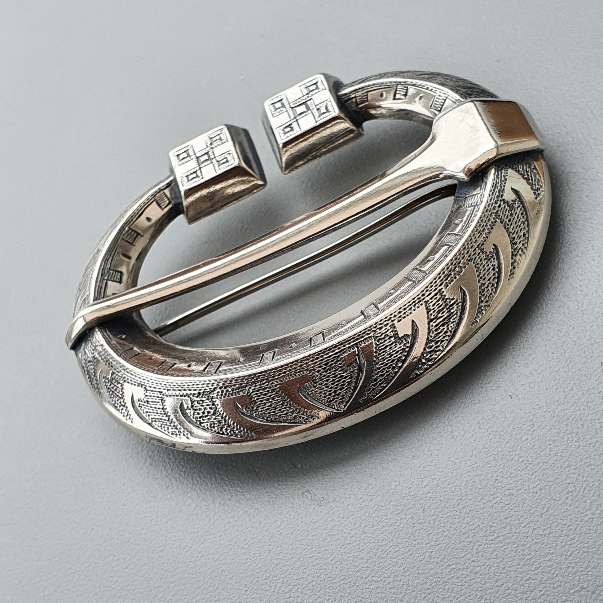 Ornate silver penannular brooch with engraved patterns and square end terminals.