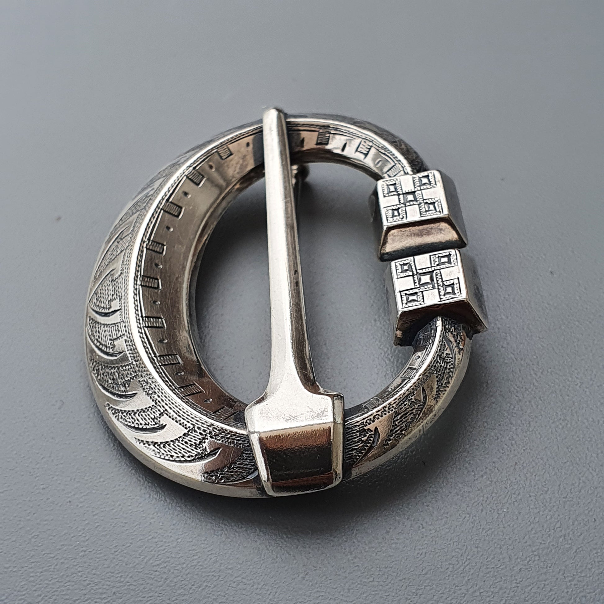 Ornate silver brooch or buckle with intricate engraved patterns and geometric designs.