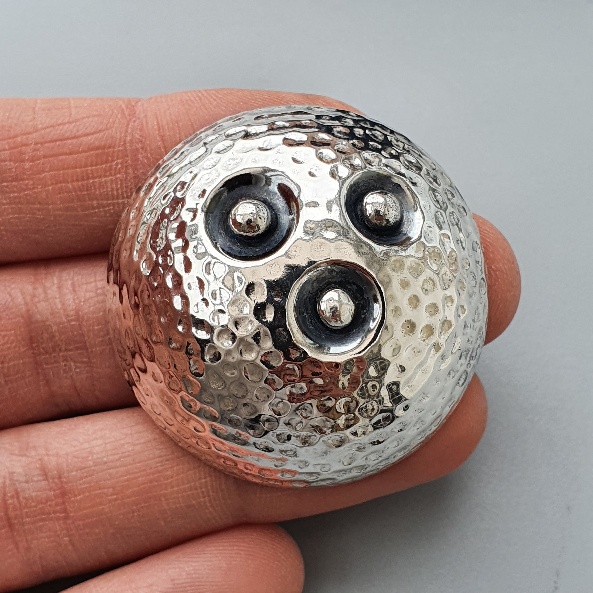 Metallic spherical object with a dimpled surface and three circular indentations resembling eyes and a mouth.