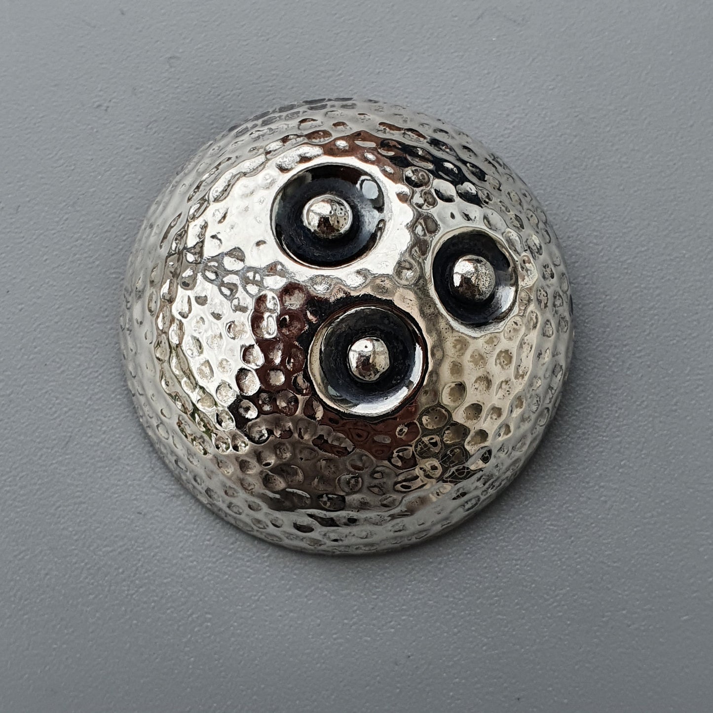 Metallic spherical object with a hammered texture and three circular indentations.