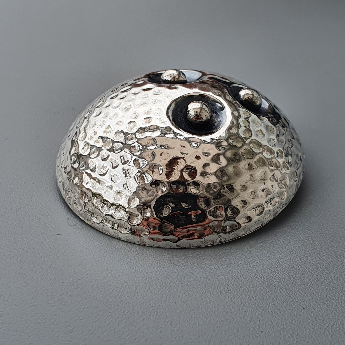 Hammered metal dome with smooth spherical protrusions on its surface.