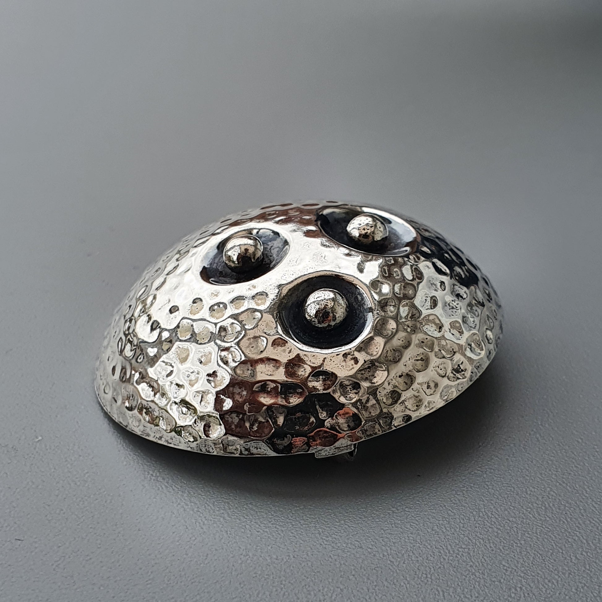 Metallic, textured dome-shaped object with three dark circular indentations on top.