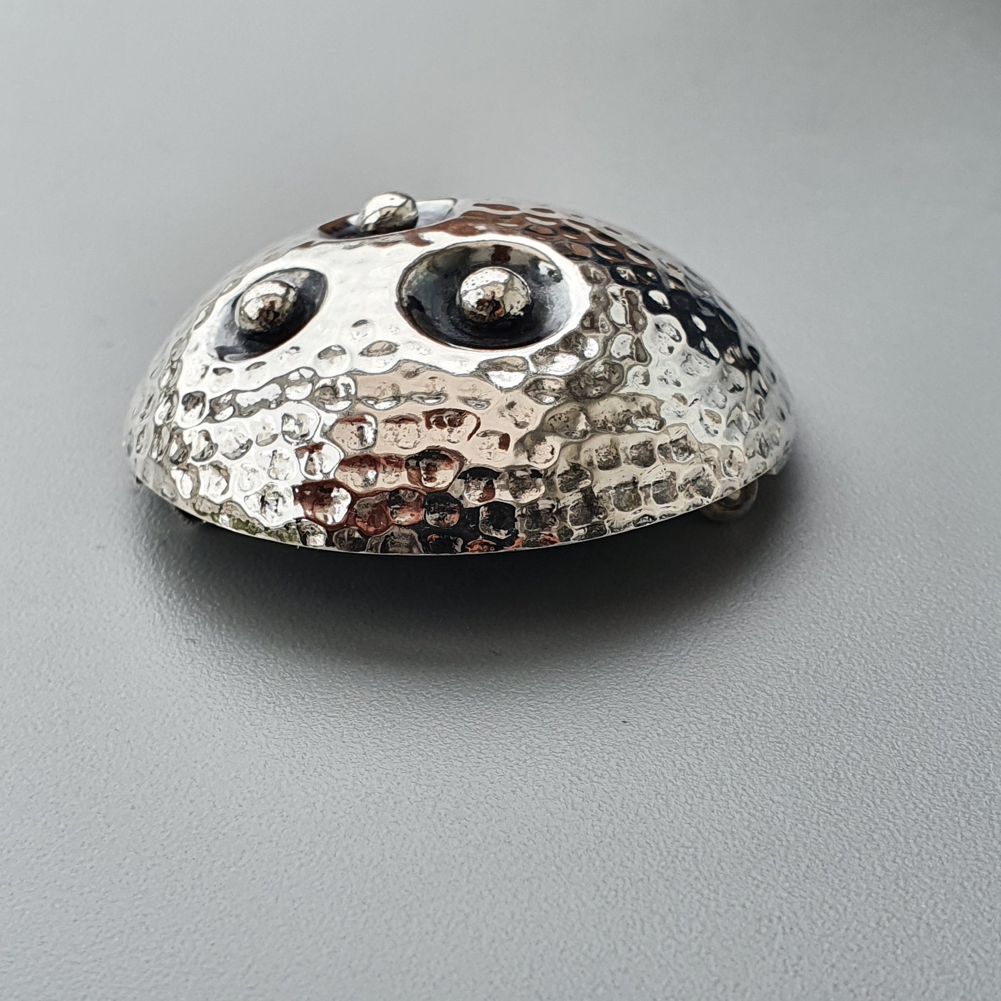 Metallic, dome-shaped object with two protruding eyes and a textured surface resembling a stylized creature or character.