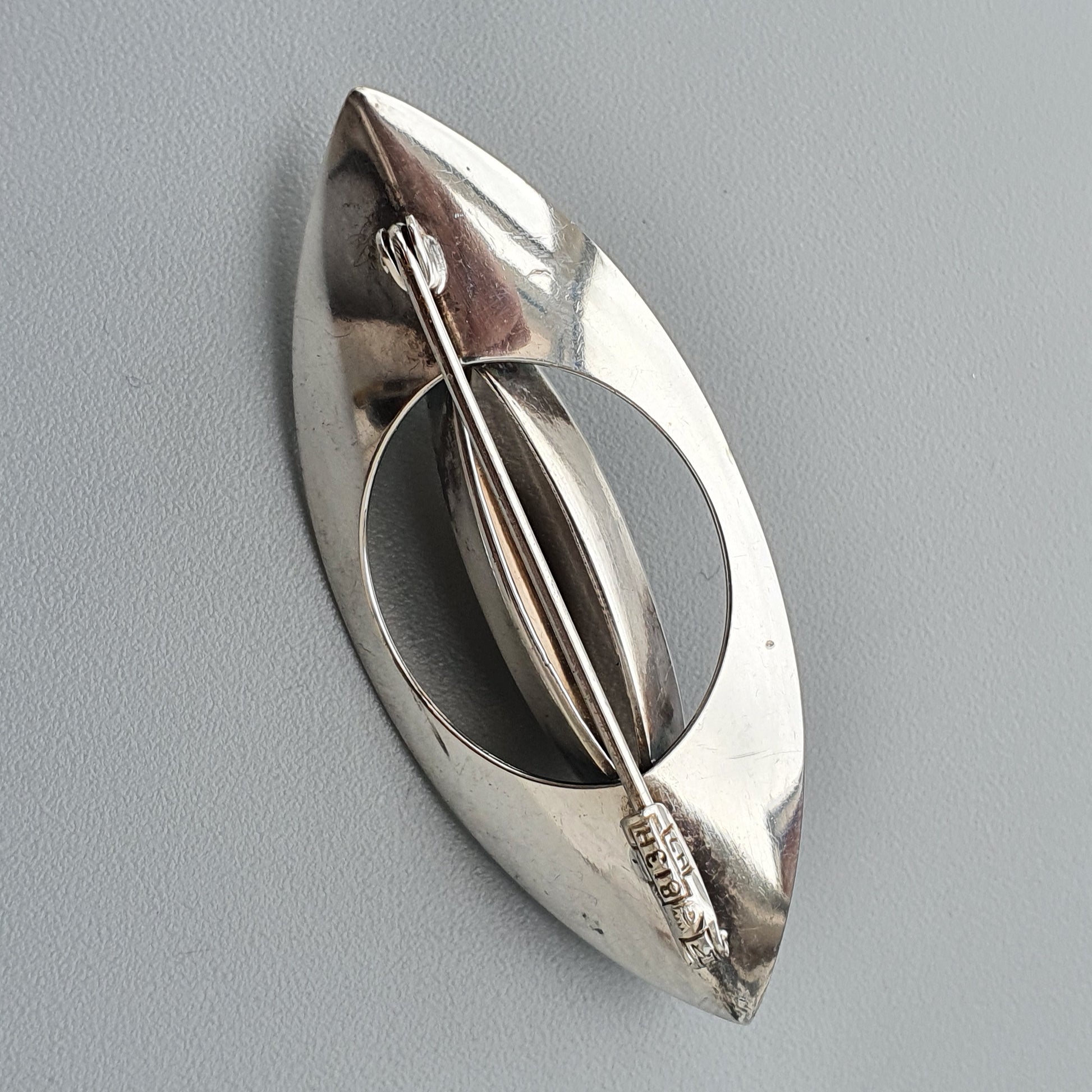 Silver brooch or pin with an oval shape and a central bar design.