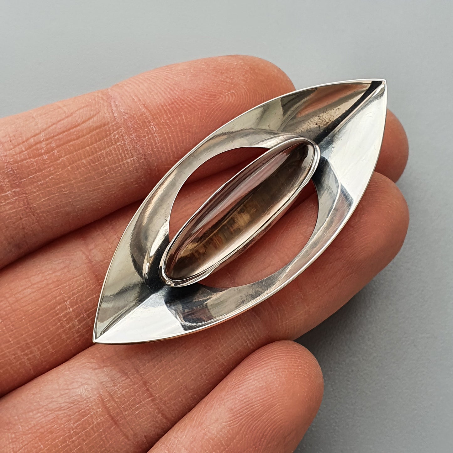 Sleek, eye-shaped silver brooch or pendant with an oval cutout in the center.