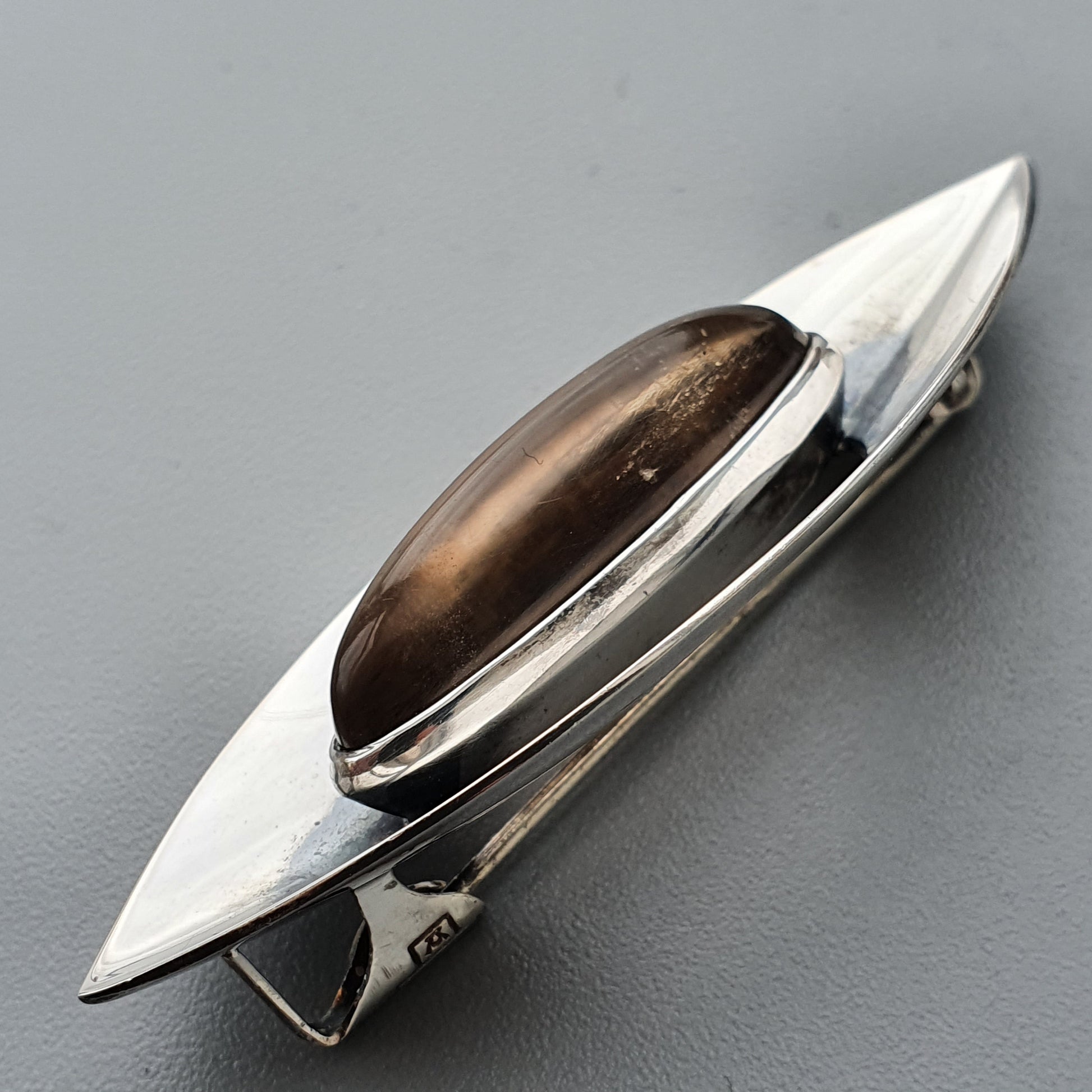 Sleek silver brooch with an elongated teardrop shape and a brown gemstone centerpiece.