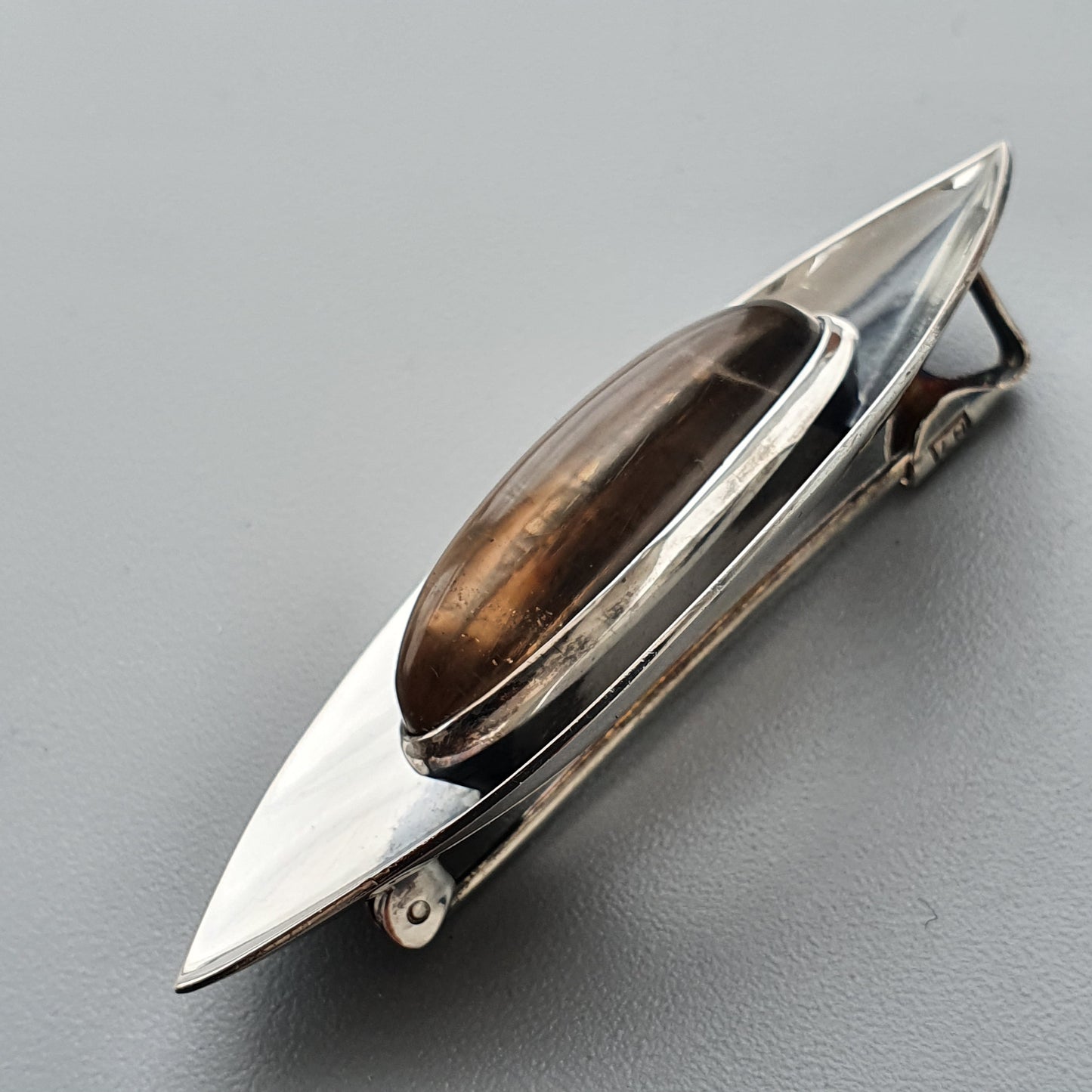 Sleek silver brooch with an elongated teardrop shape and brown gemstone inlay.