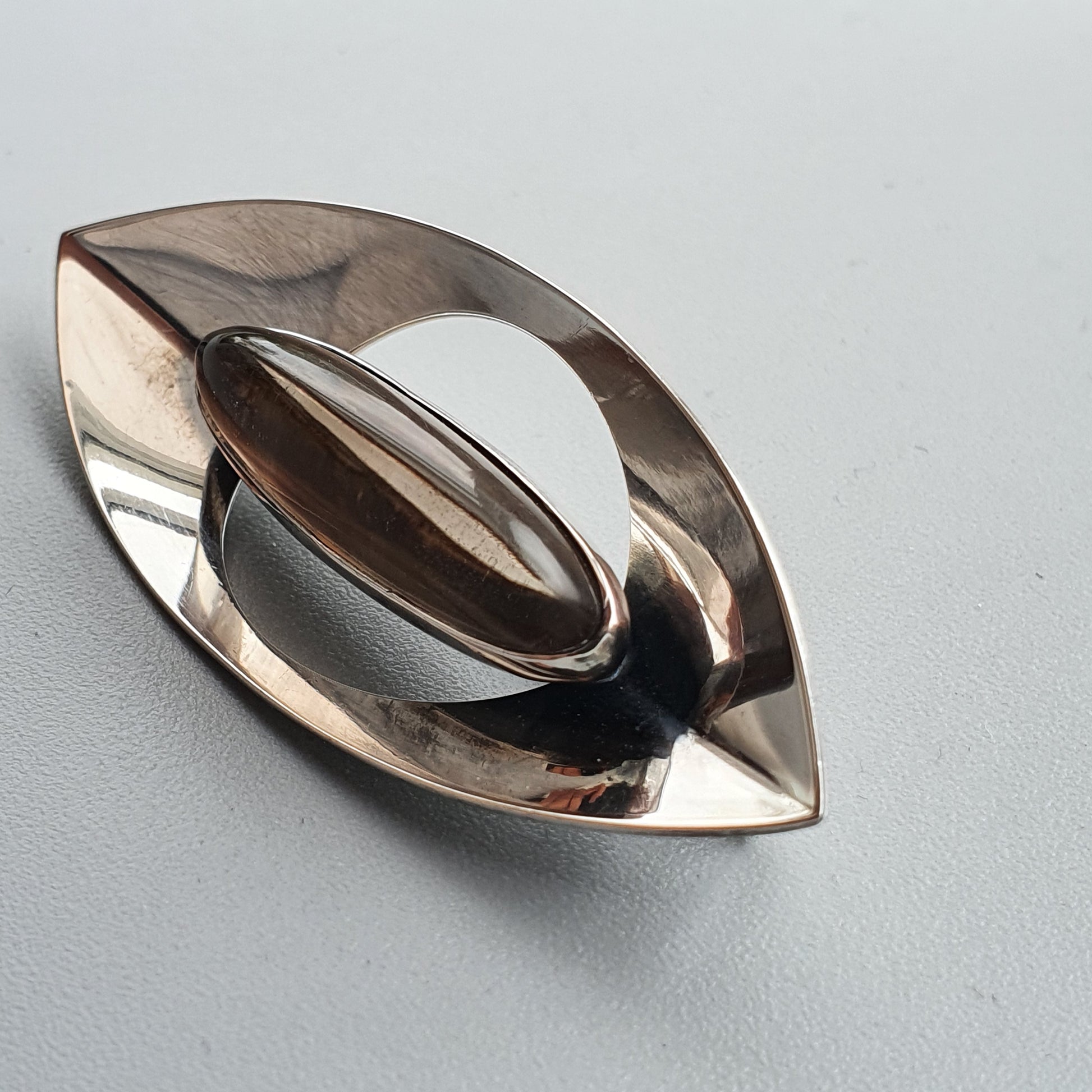 Metallic, eye-shaped object with a reflective surface and an oval cutout in the center.