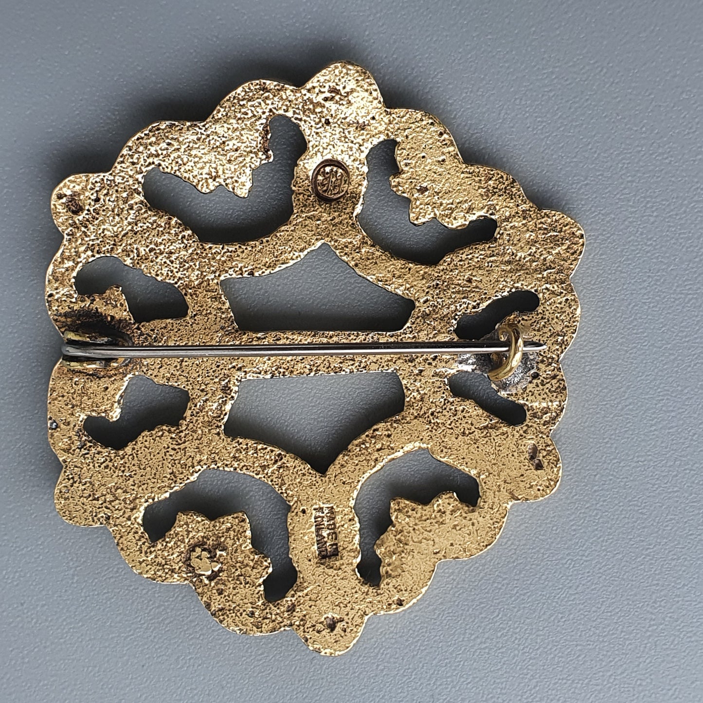 Gold-colored ornate brooch or pin with intricate cutout designs.