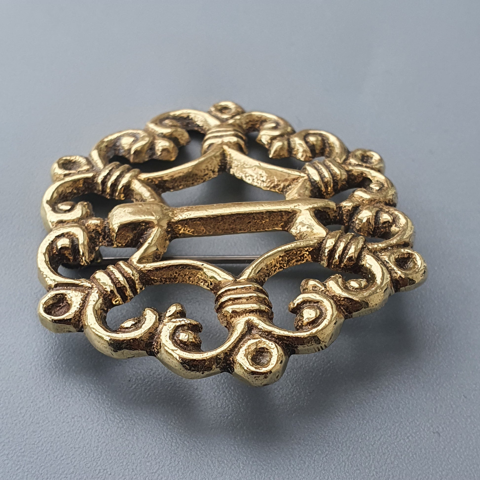 Ornate gold-colored brooch with intricate swirling patterns and floral motifs.