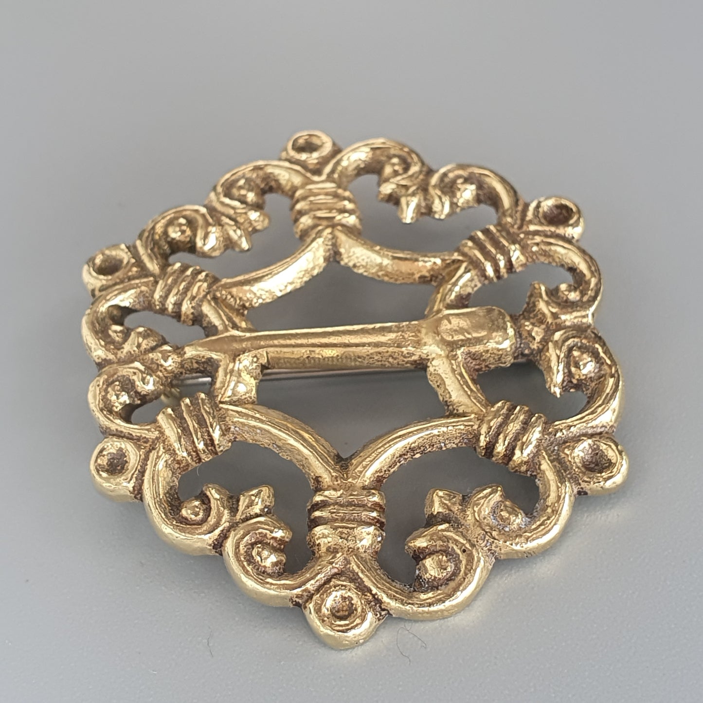 Ornate gold-colored brooch with intricate scrollwork and a central bar design.