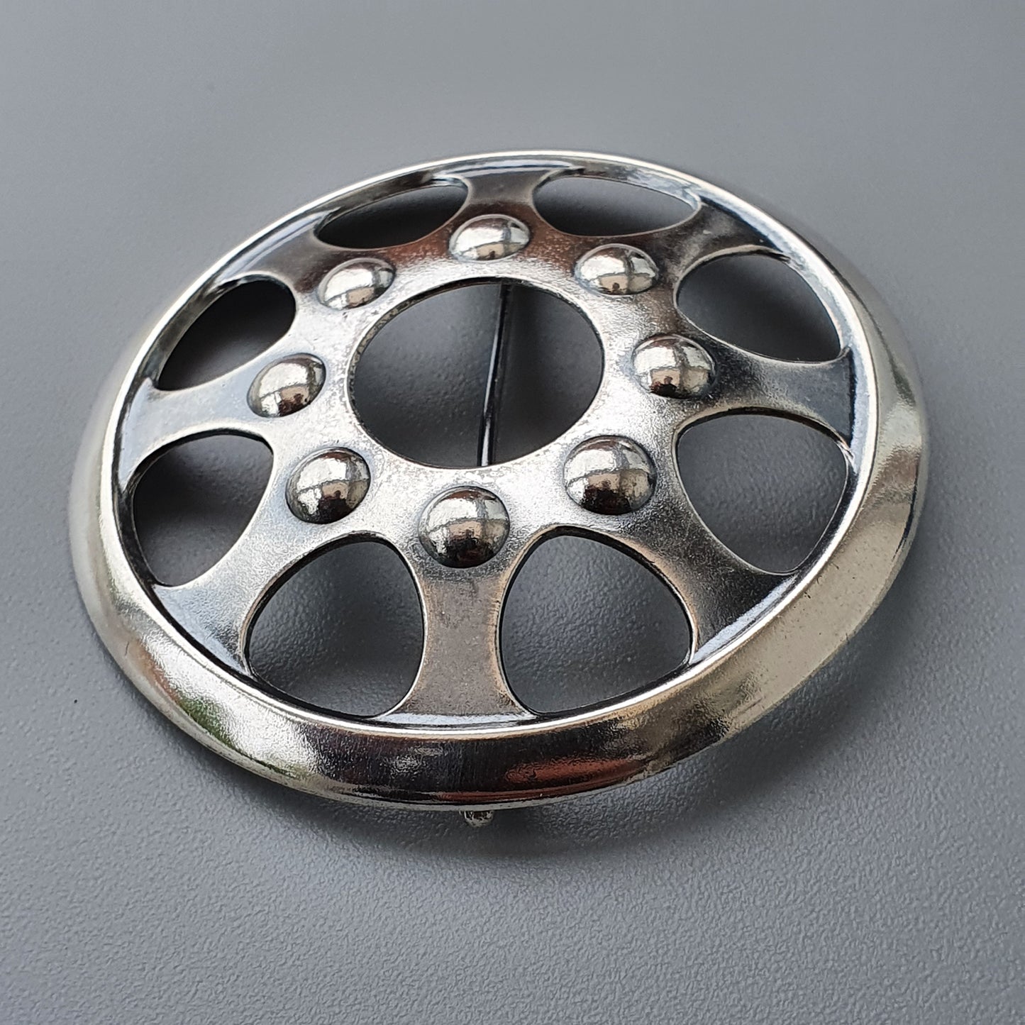 Metallic wheel cover or hubcap with circular cutouts and raised spherical accents.