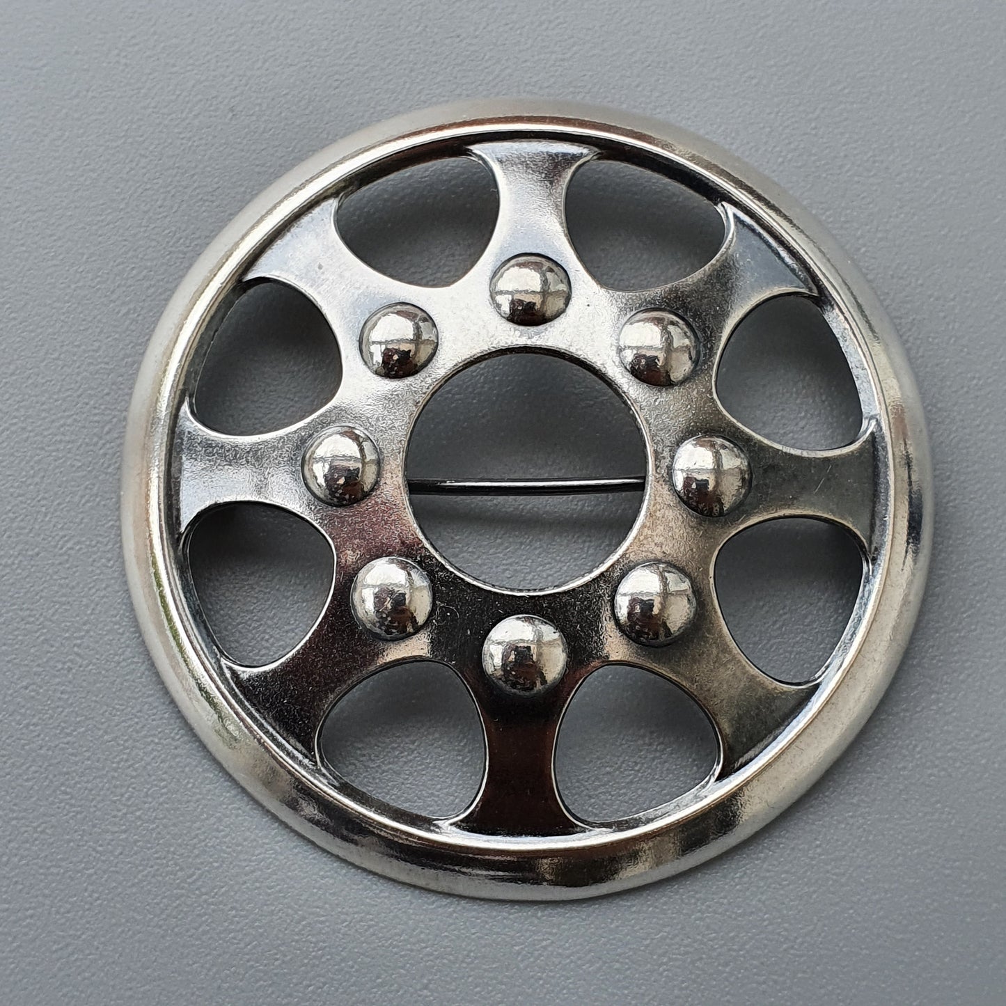 Circular metal wheel cover or hubcap with decorative holes and spherical studs.