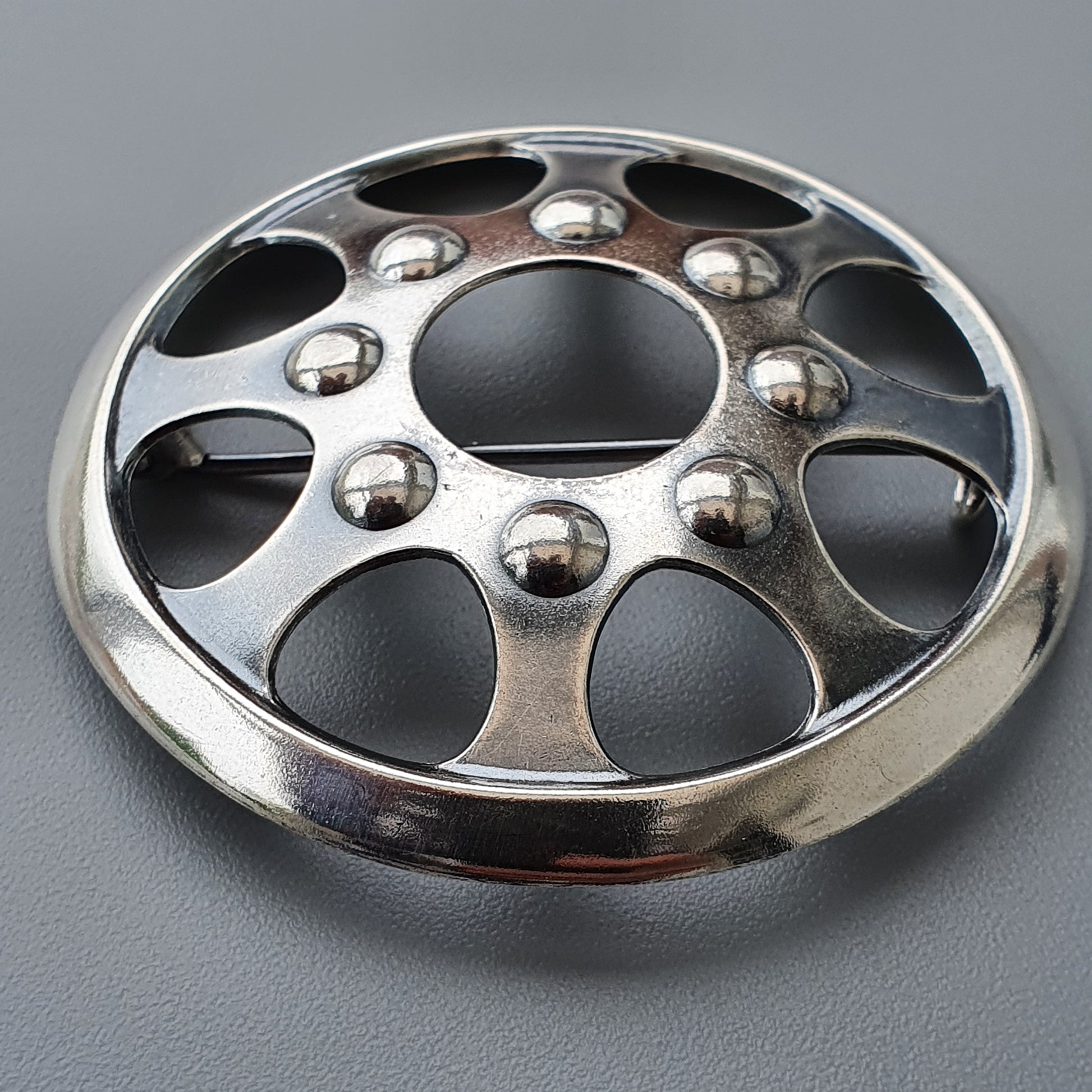 Metallic wheel rim or hubcap with circular cutouts and spherical decorations.