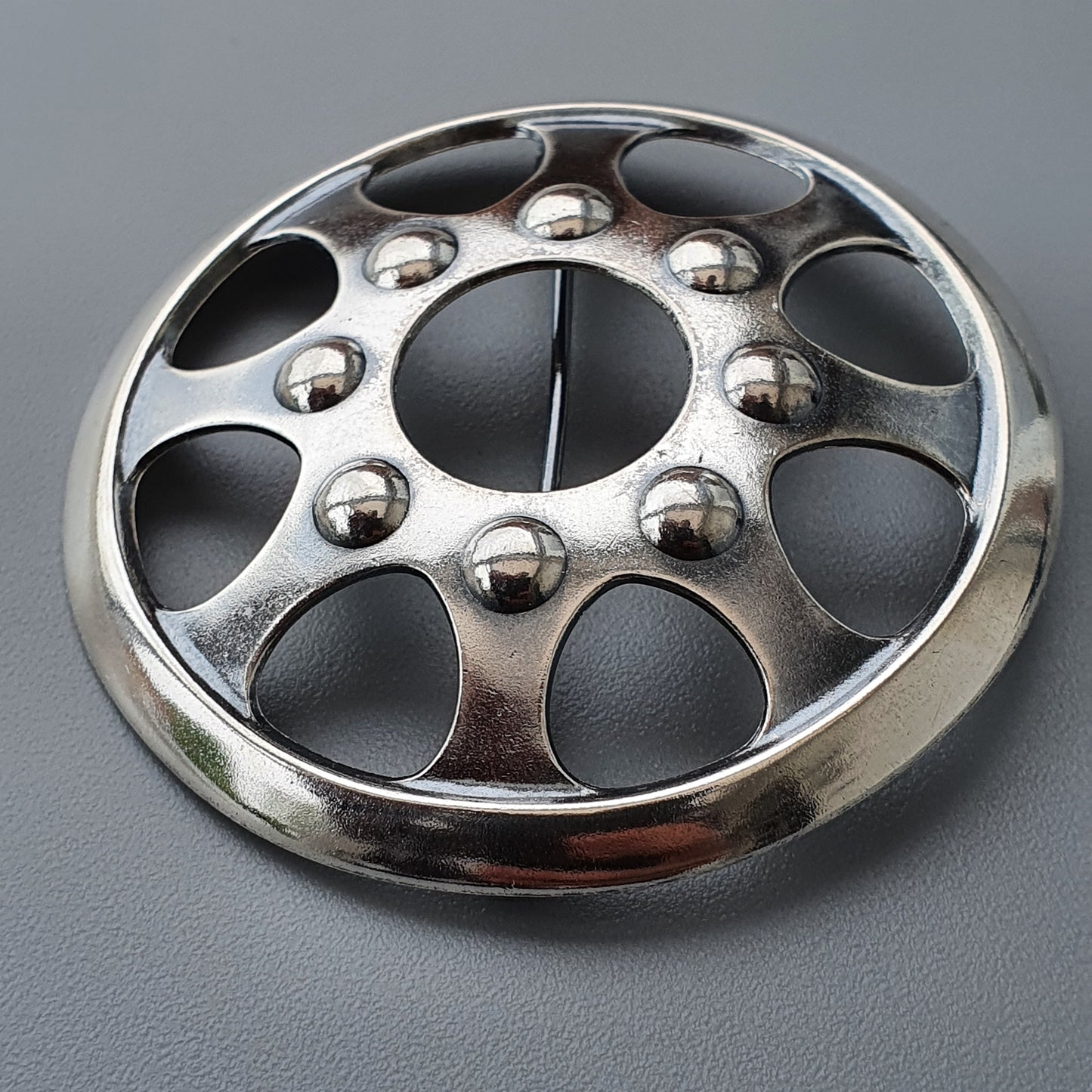 Metallic wheel cover or hubcap with circular cutouts and raised spherical accents.