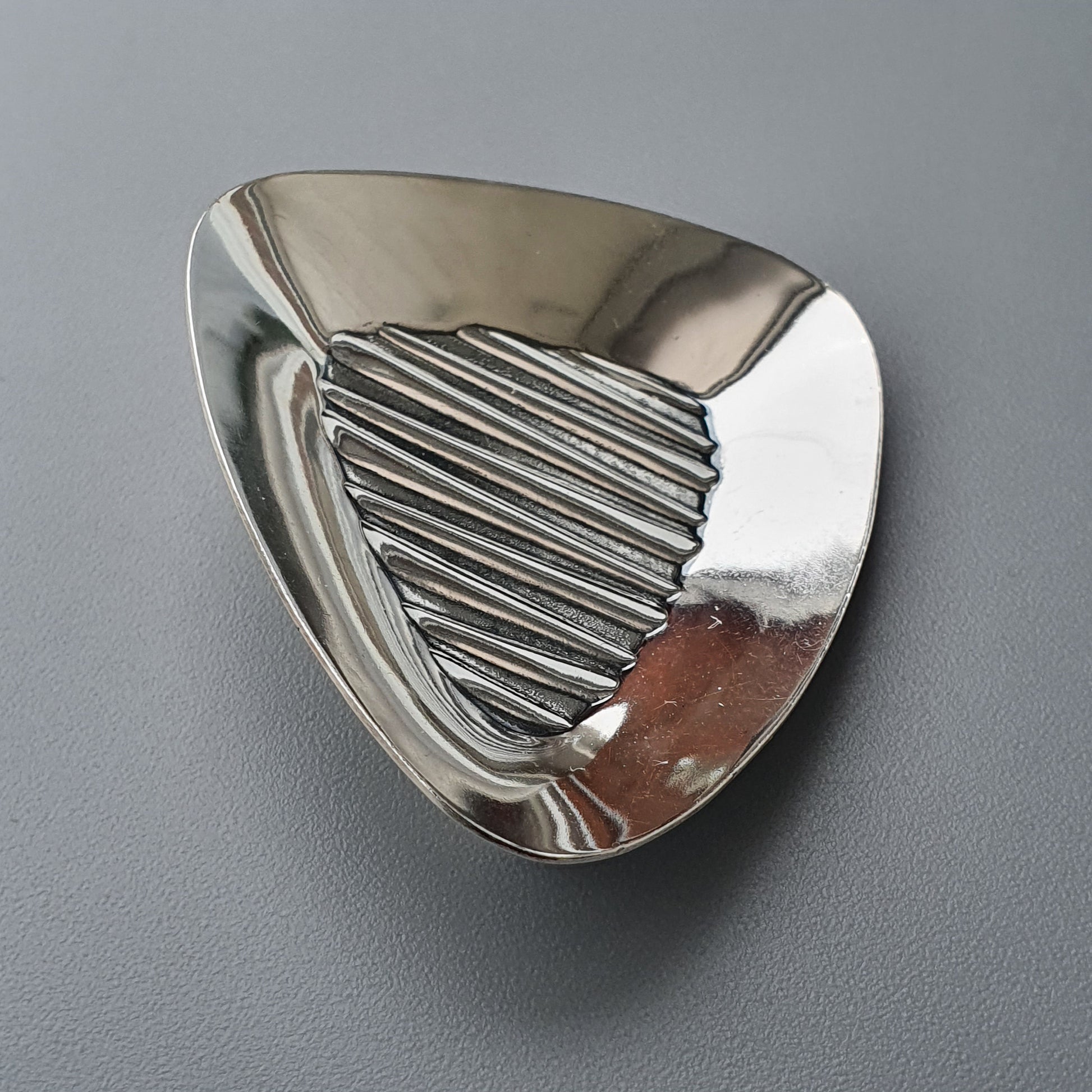 Triangular silver brooch or pin with ridged texture on one section.