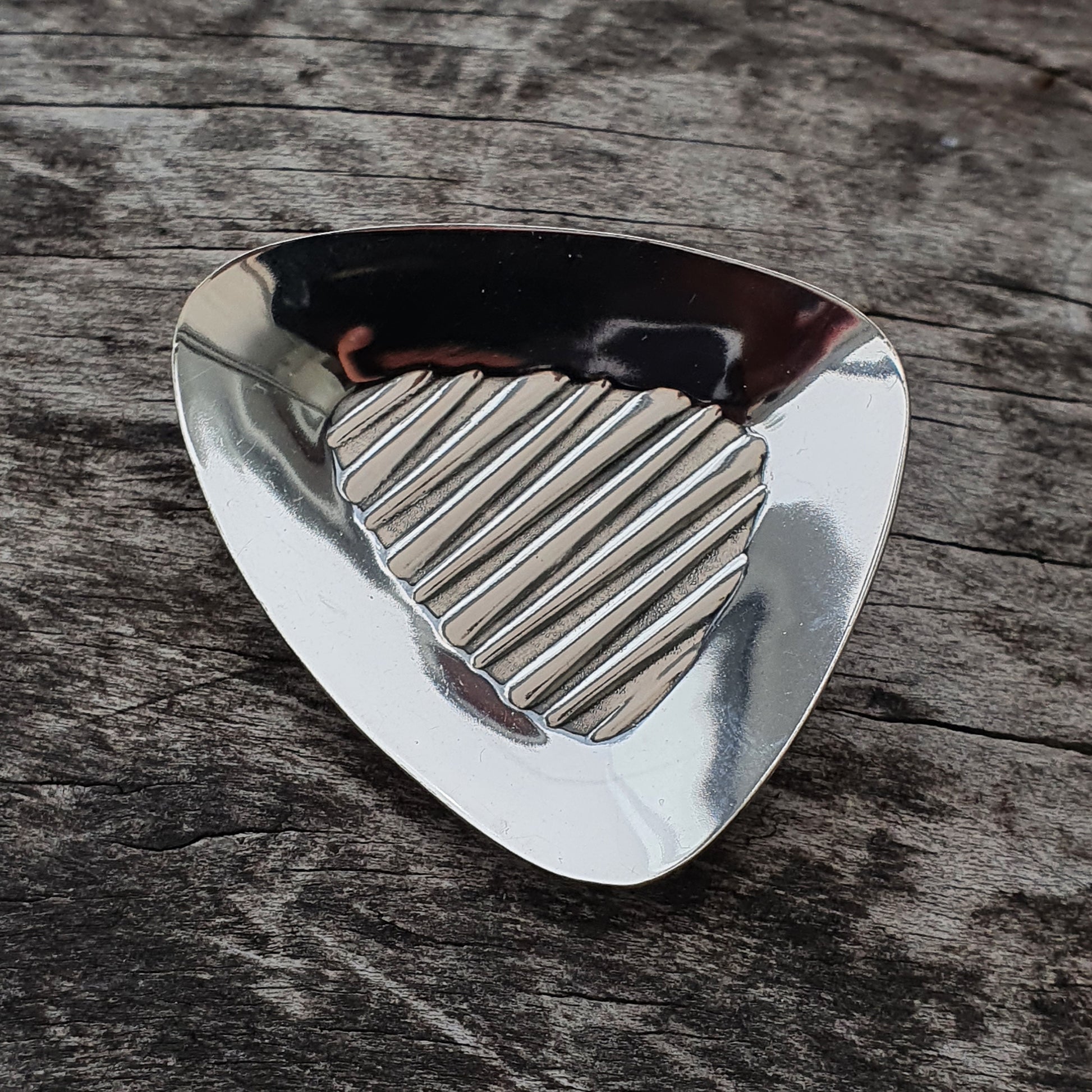 Guitar pick made of metal with a ribbed surface pattern.