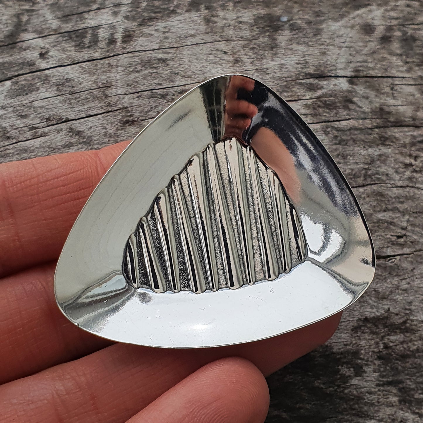 Triangular metal guitar pick with a textured grip pattern.