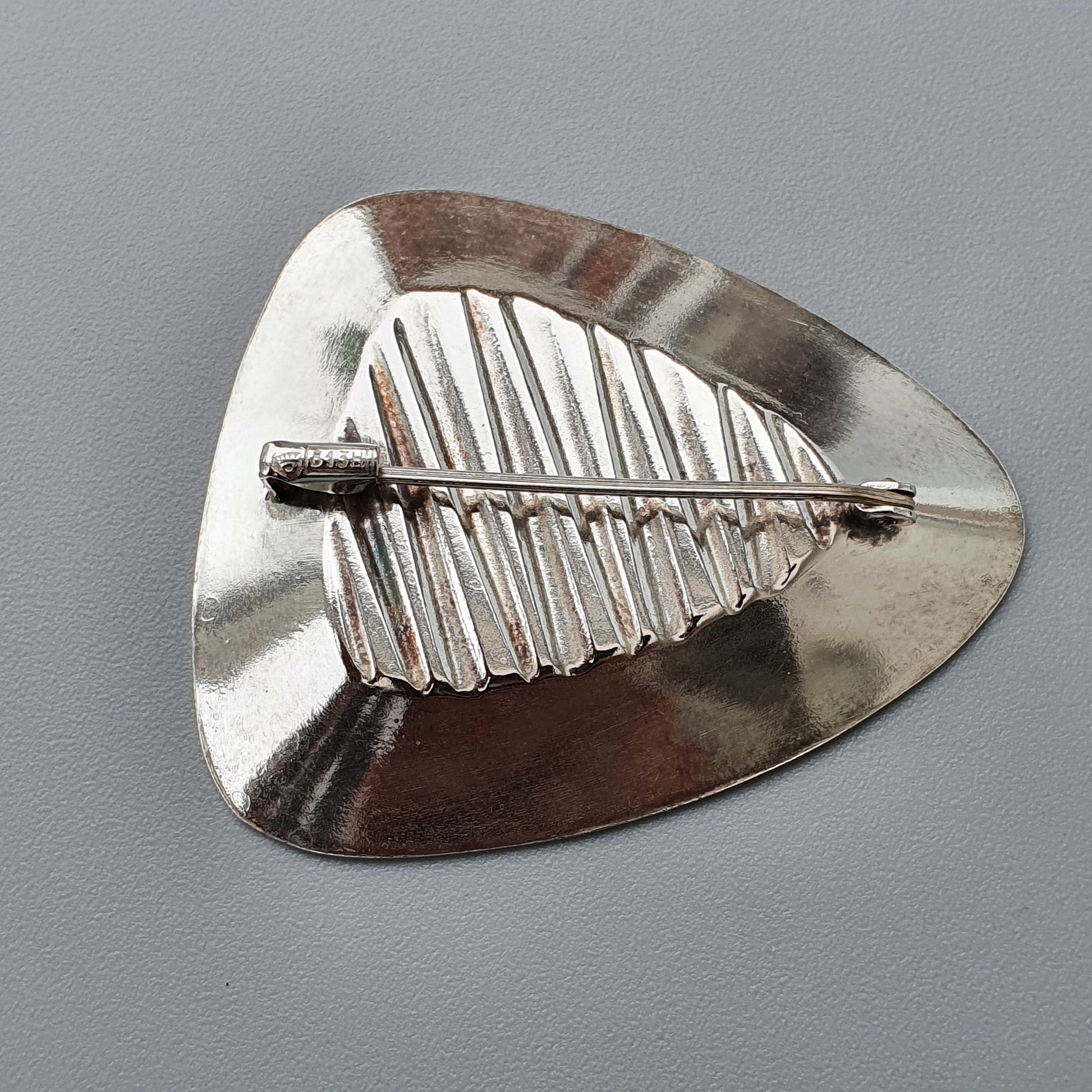 Silver guitar pick with an embossed leaf design.