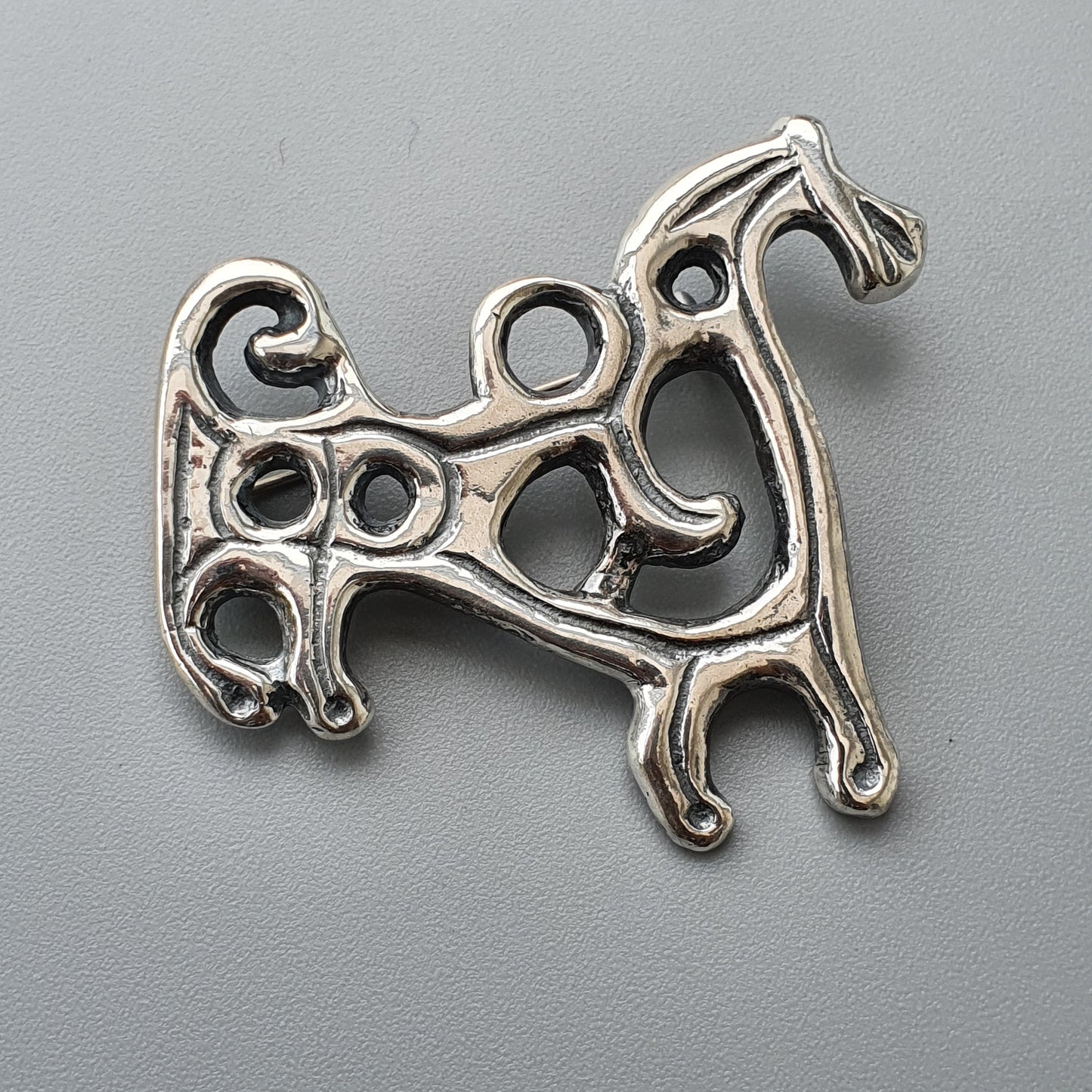 Silver pendant shaped like a stylized dog or animal figure with curving lines and circular openings.