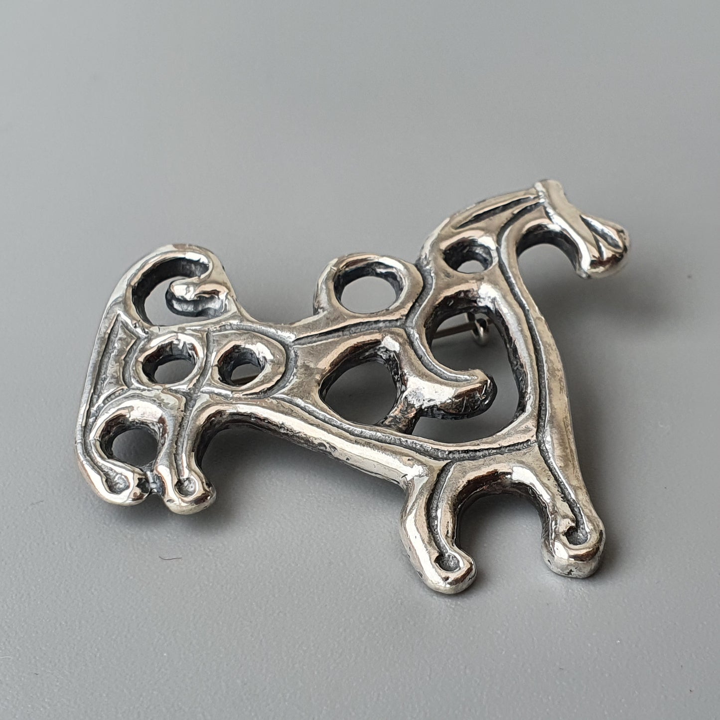 Silver-colored decorative brooch or pendant shaped like a stylized dog with intricate openwork design.