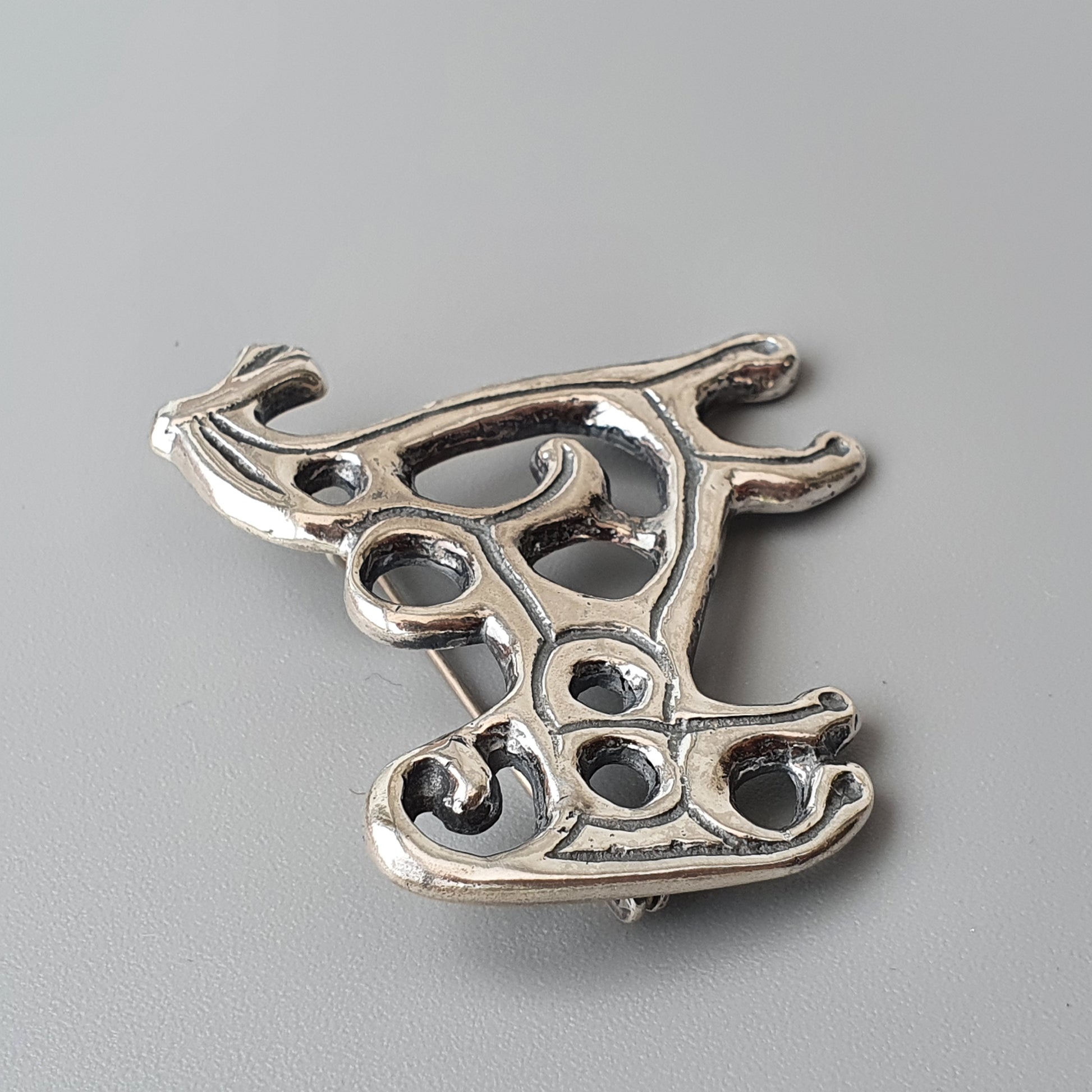 Silver-colored abstract brooch or pendant with an intricate openwork design resembling organic shapes.