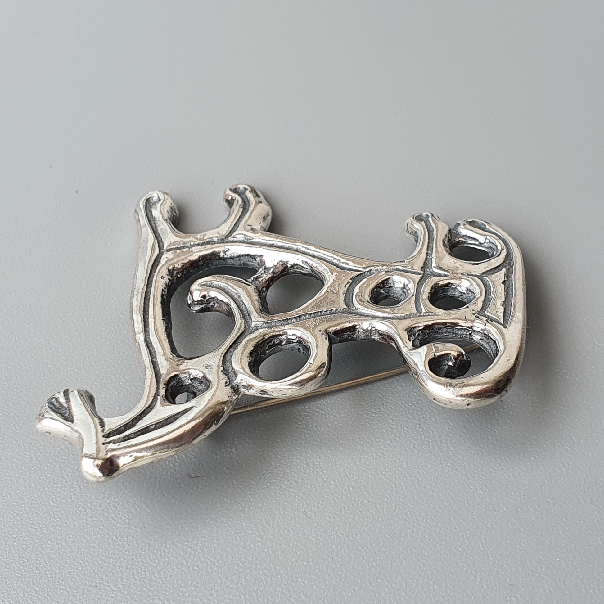 Ornate silver brooch or pin with a curving, organic design featuring openwork patterns.