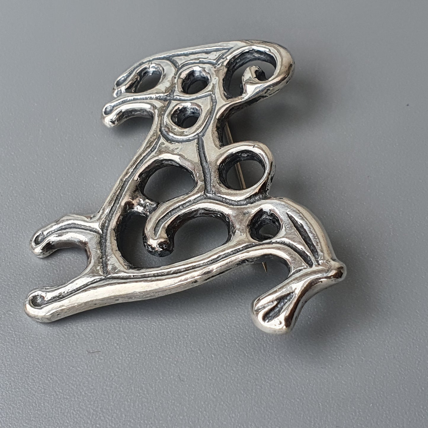 Ornate silver brooch or pendant with an abstract, curvilinear design resembling stylized animal or plant forms.