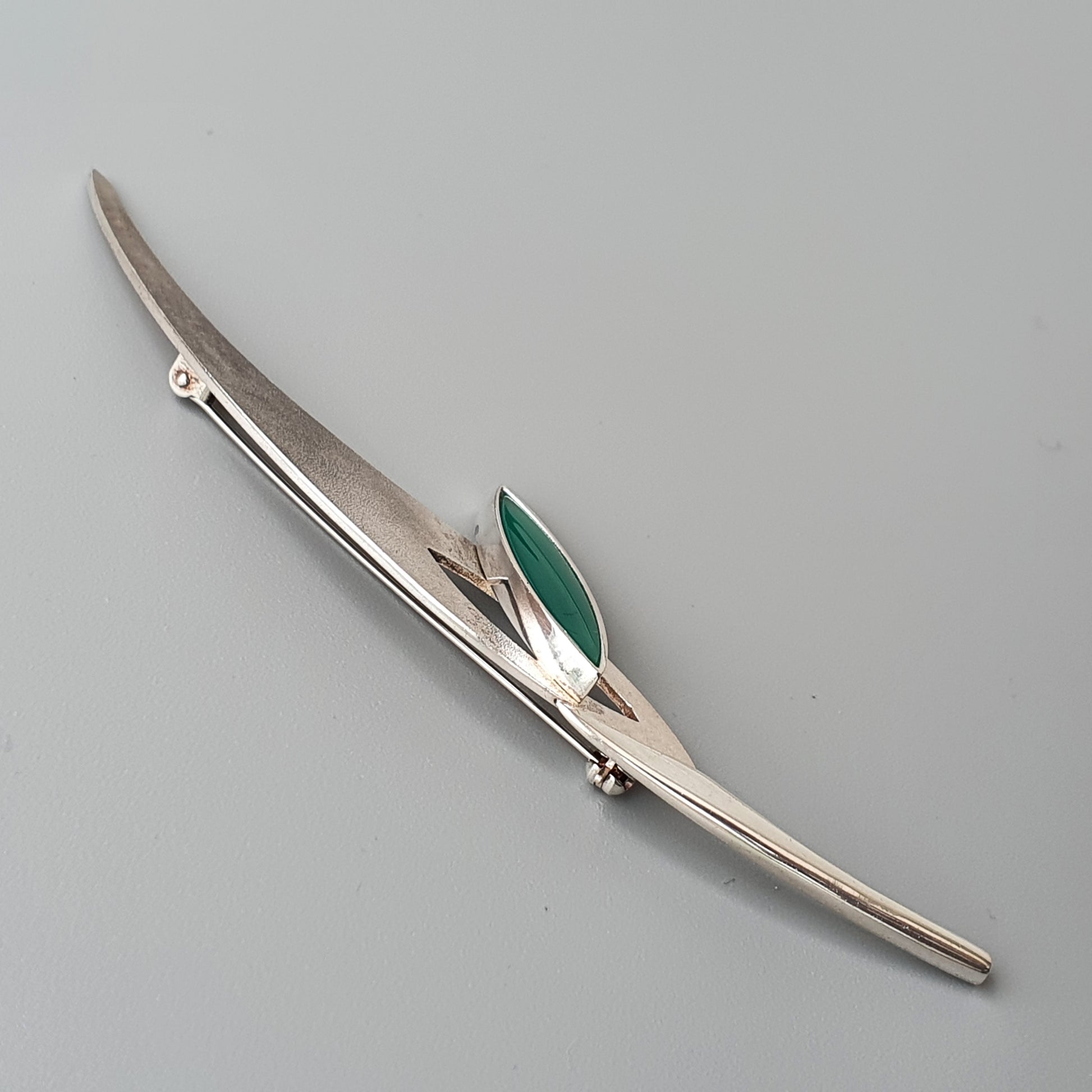 Sleek silver brooch with an elongated shape and green accent.