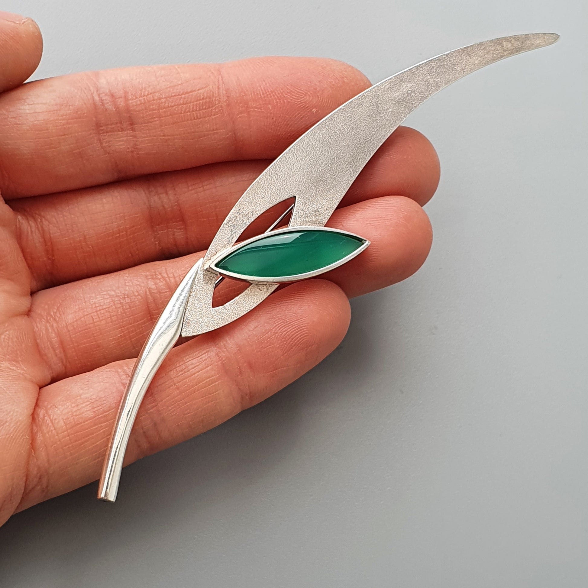 Silver brooch or pin shaped like a stylized leaf with a green gemstone accent.