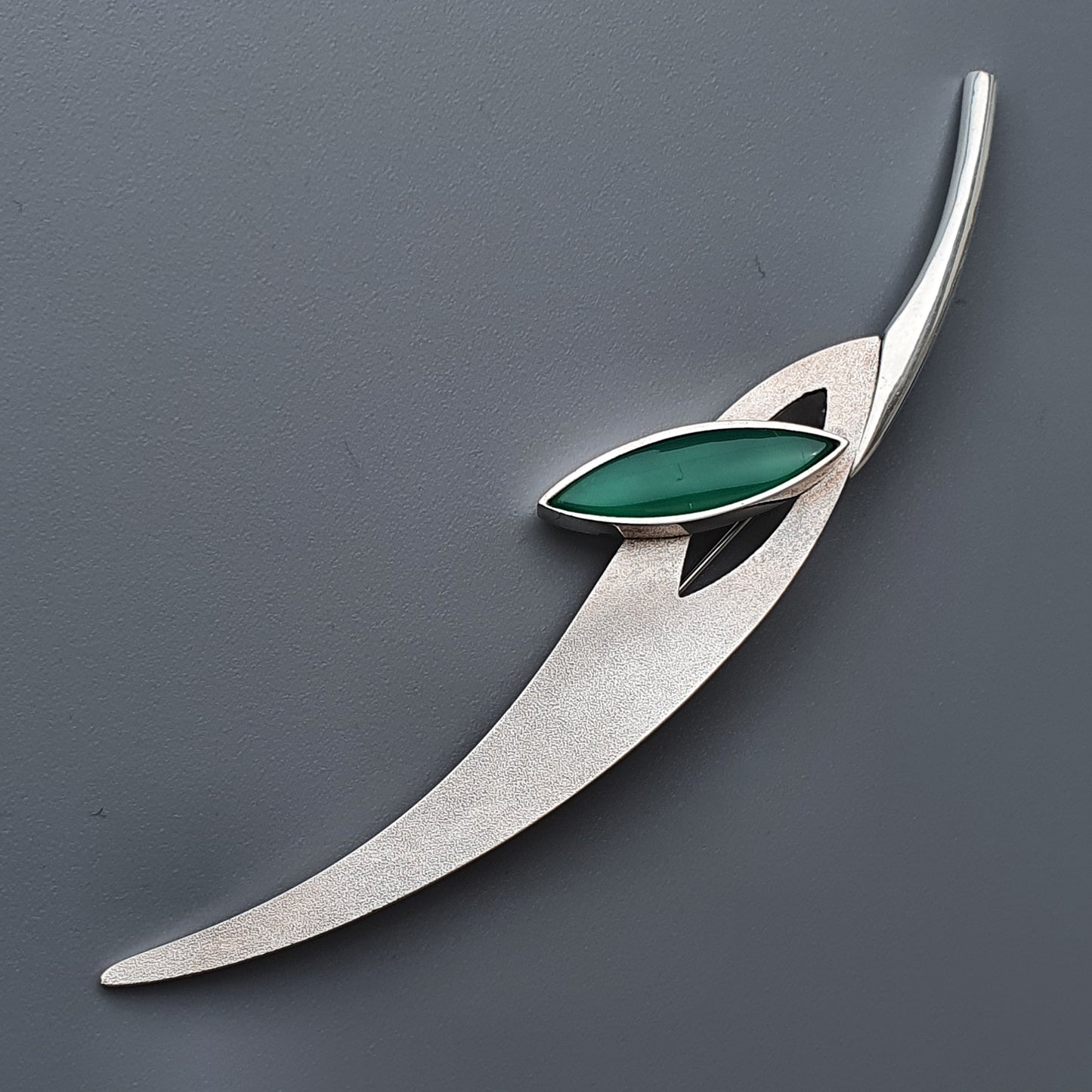 Sleek silver brooch with a curved shape and green gemstone accent.