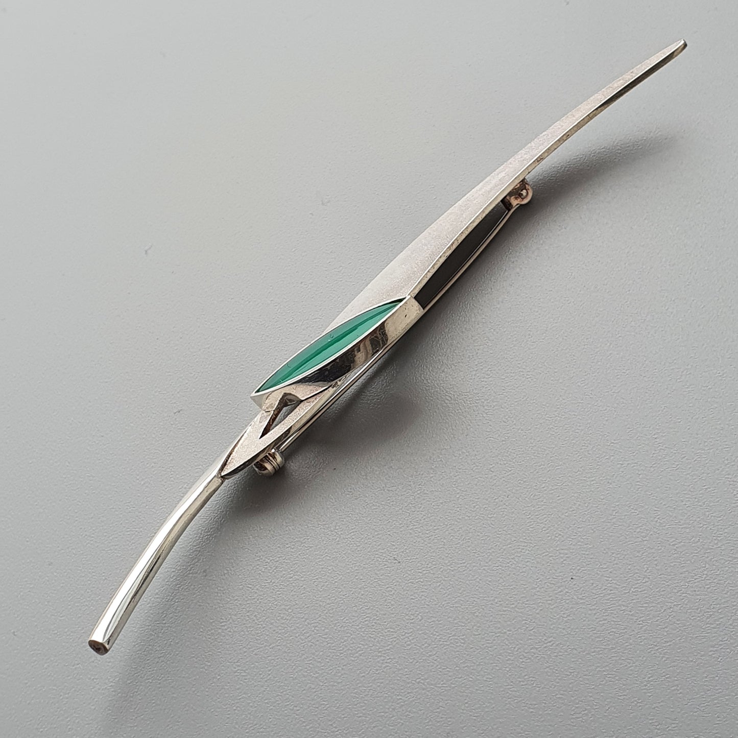 Sleek, elongated silver brooch with a green inlay accent.