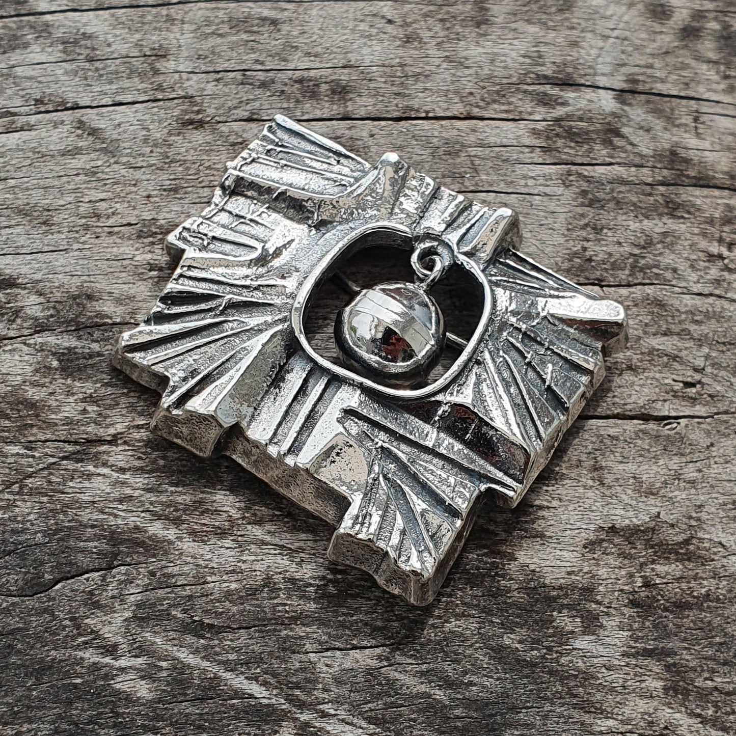 Silver pendant shaped like a stylized sun or compass rose with a central circular design.