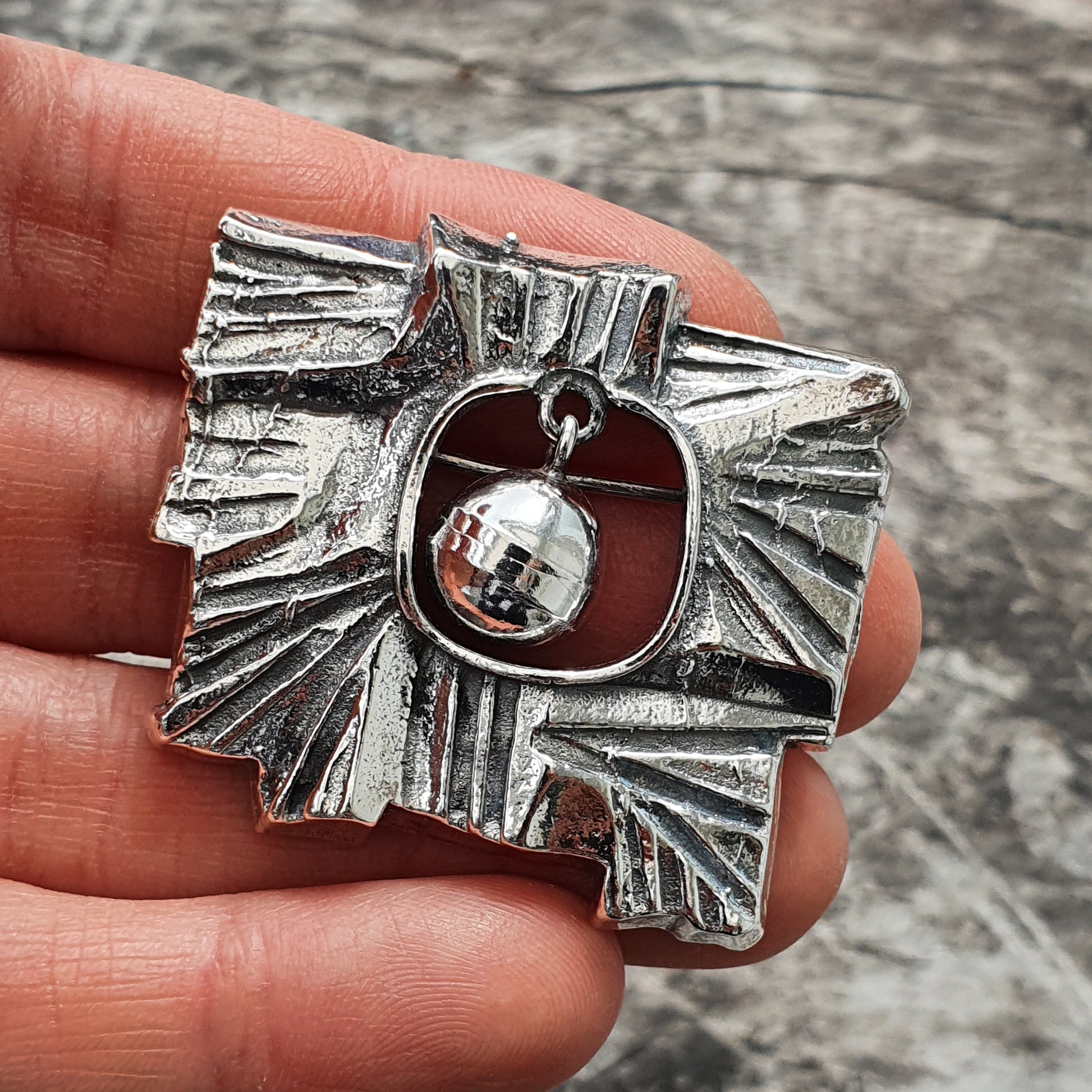 Ornate silver brooch or pendant with an abstract geometric design and a dangling spherical charm.