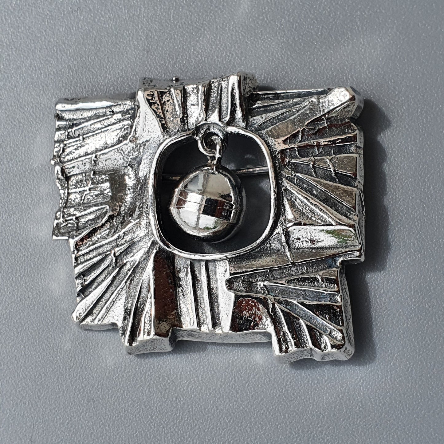 Silver abstract brooch or pendant with a dangling crystal-like element in its center.