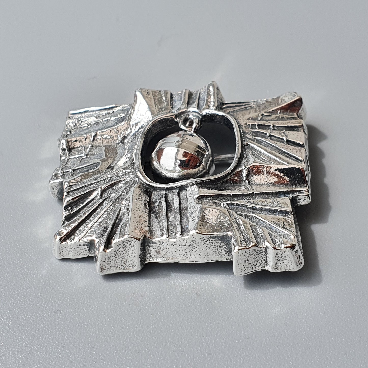 Silver abstract brooch or pendant with a central spherical element surrounded by angular geometric shapes.