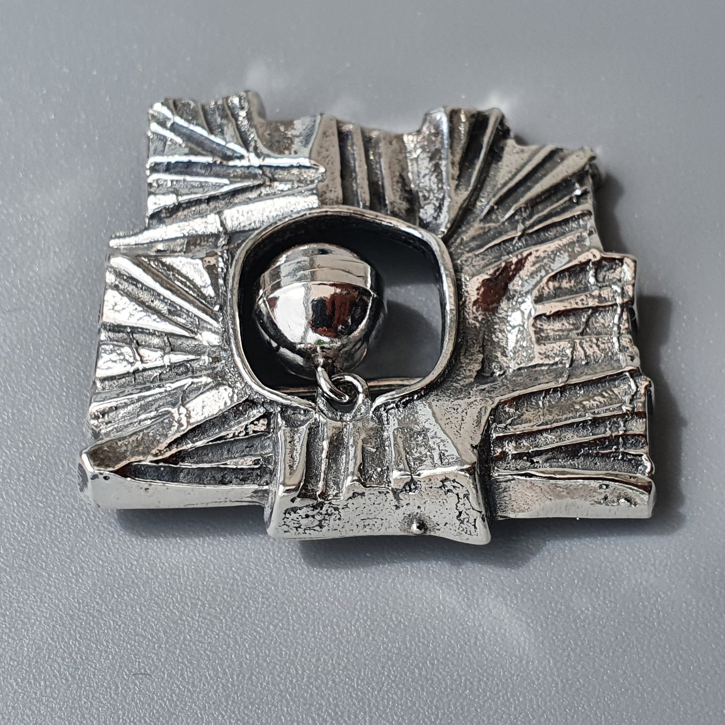 Silver brooch or pendant with an abstract, textured design surrounding a central spherical element.