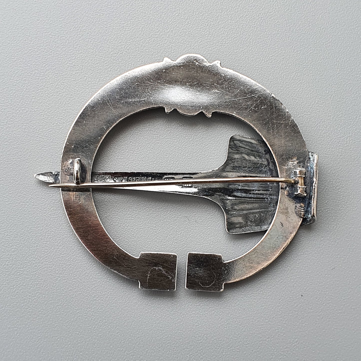 Silver circular brooch with a fish-shaped design and a pin clasp.