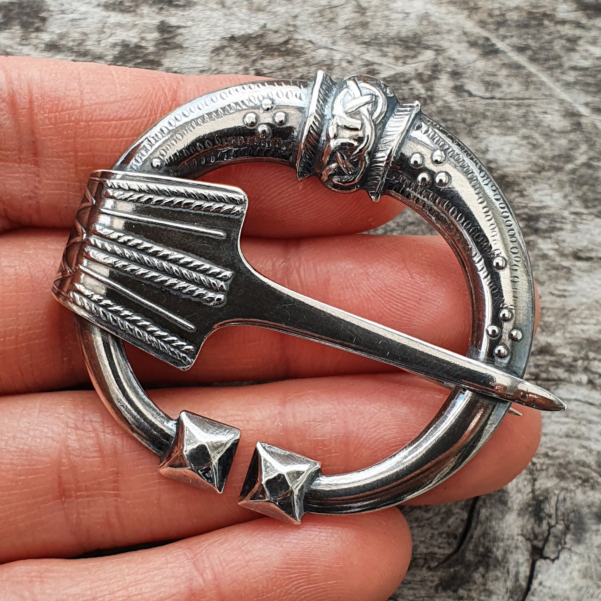 Ornate silver brooch shaped like a circular Celtic-style pin with an axe or hammer design.