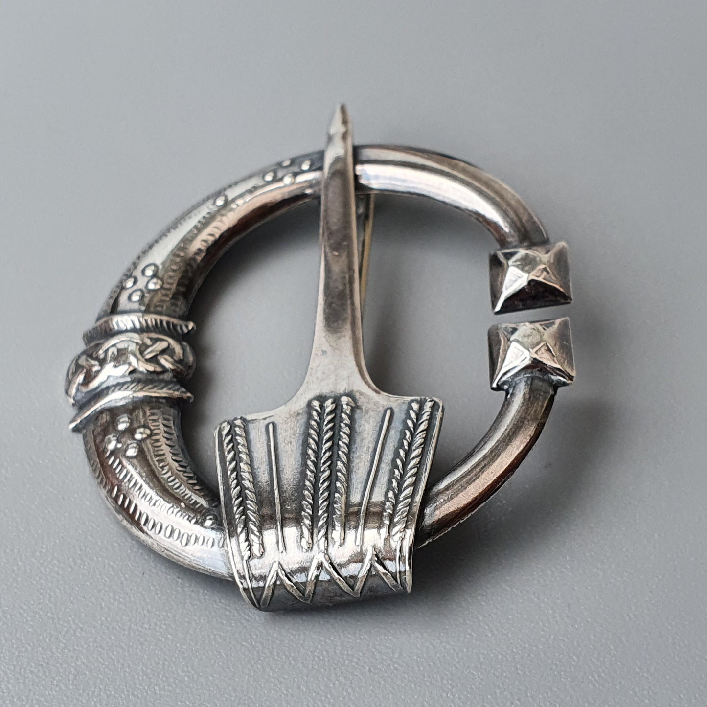 Ornate silver penannular brooch with intricate Celtic-style engravings and decorative elements.