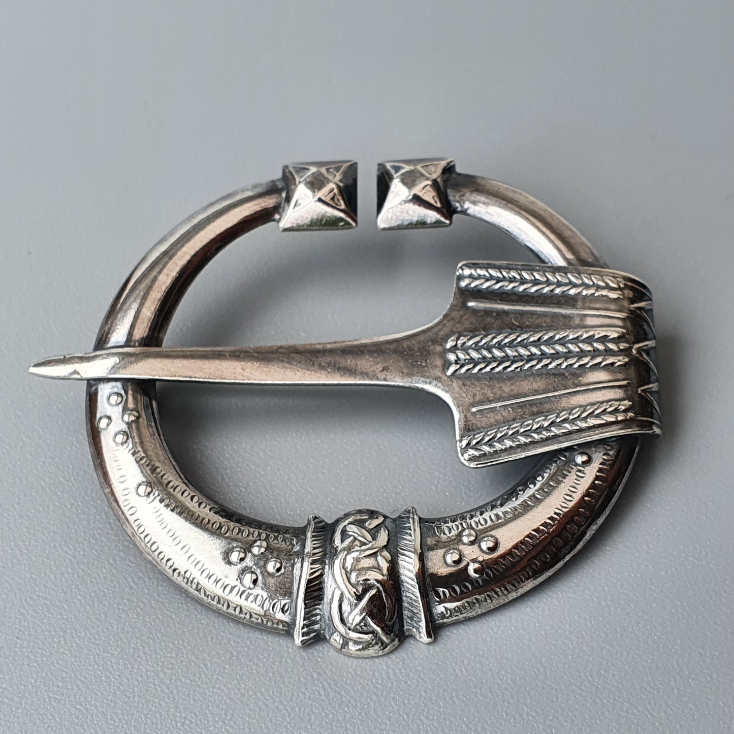 Ornate silver brooch with a pin and decorative Celtic-style engravings.