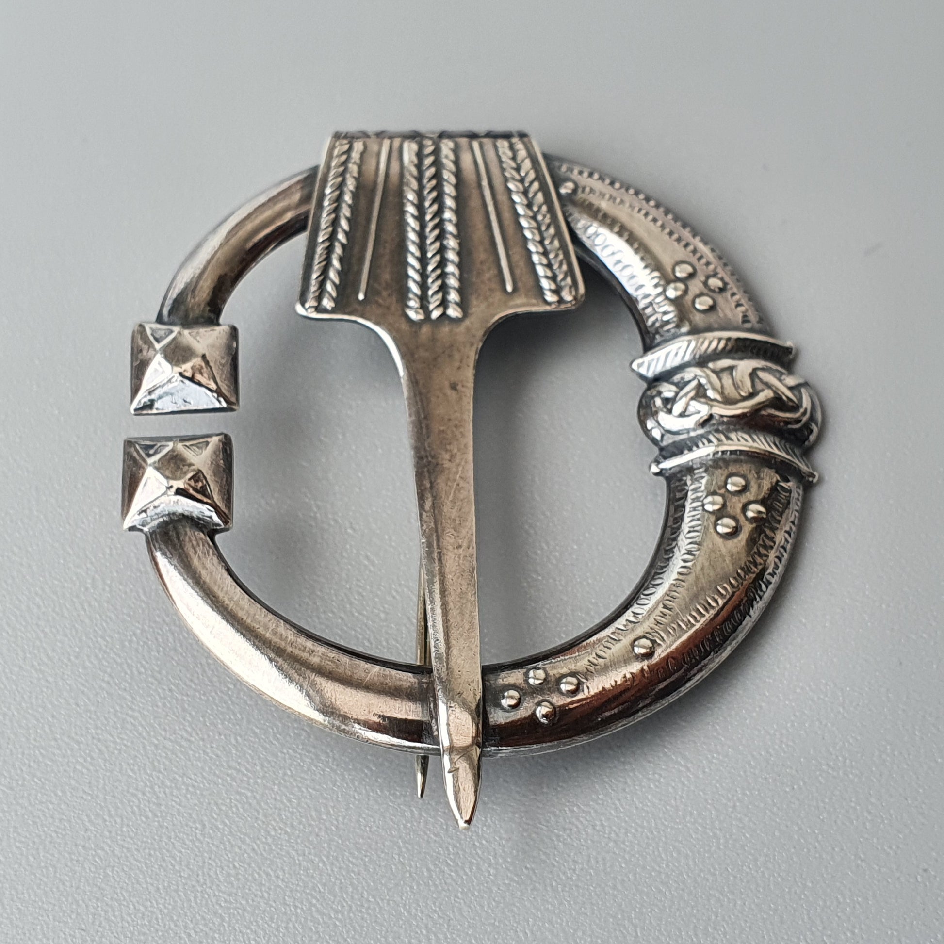 Ornate silver circular brooch with intricate Celtic-style engravings and a central pin.