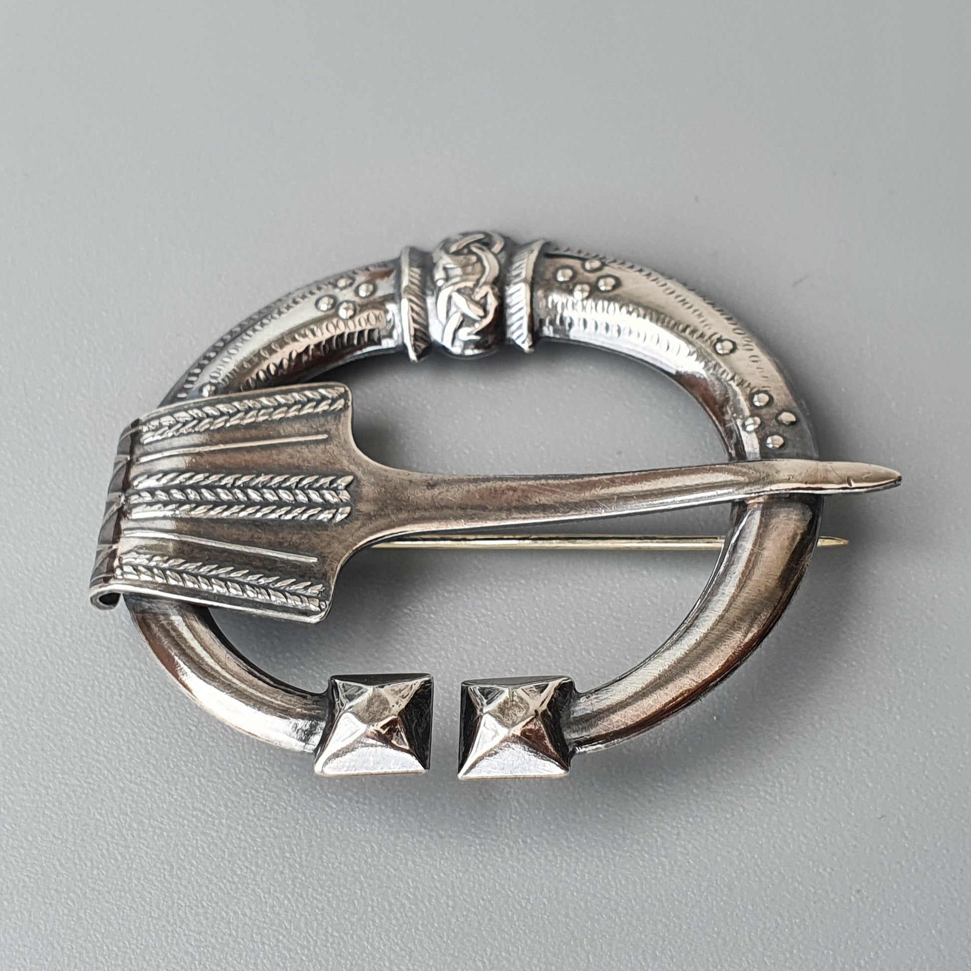 Ornate silver penannular brooch with intricate Celtic-style engravings and a pin.