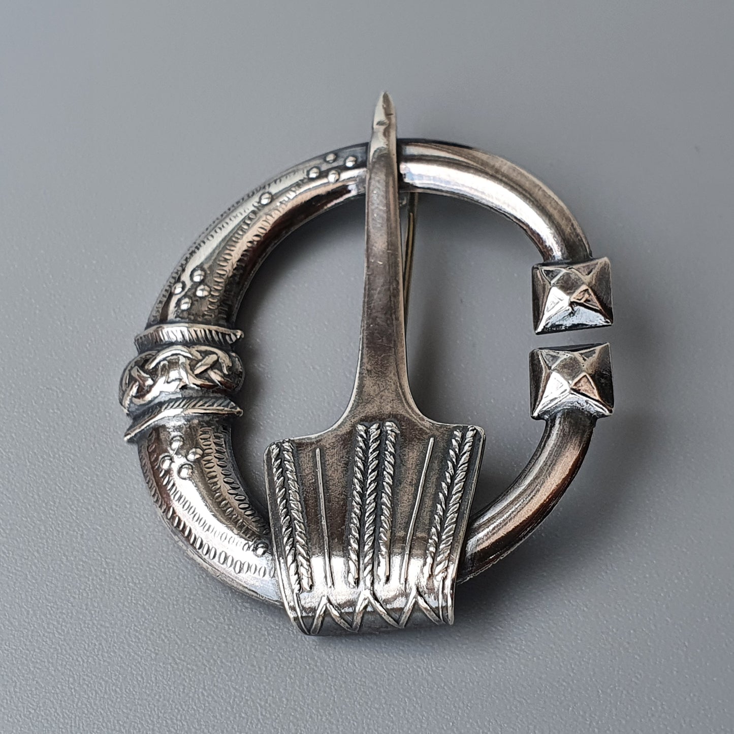 Ornate silver brooch with a circular shape and decorative pin.