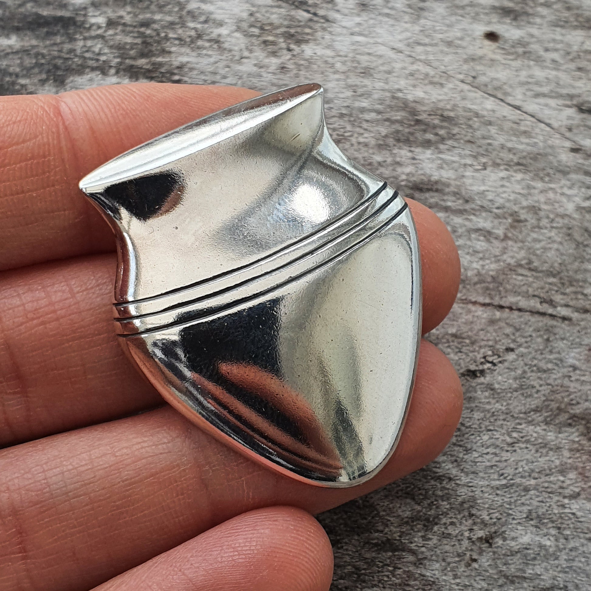 Shiny metallic guitar pick with ridged edges and a pointed tip.