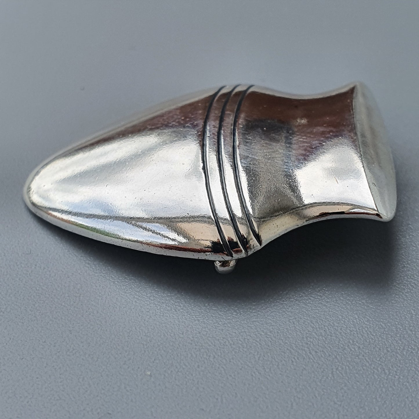 Sleek, metallic teardrop-shaped object with horizontal ridges near its wider end.