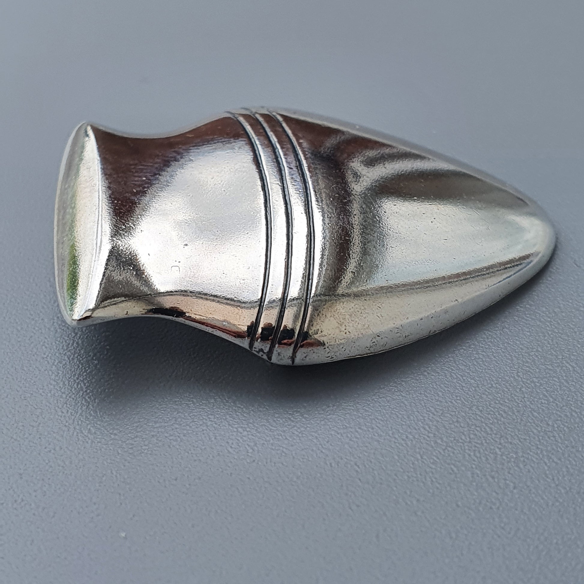 Metallic bullet-shaped object with decorative grooves around its midsection.